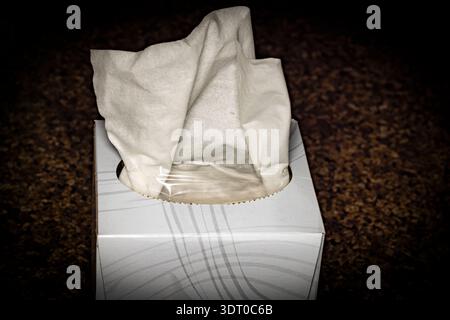Close-up of a white tissue emerging from a box on a dark surface, symbolizing hygiene, healthcare, and everyday household use Stock Photo