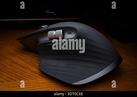 Close-up of a Logitech MX Master wireless computer mouse on a wooden desk, showing ergonomic design and precision scroll wheels Stock Photo