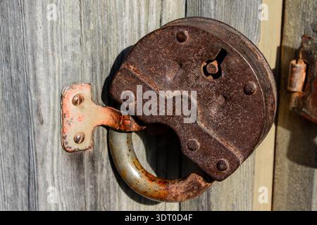 Old rusty padlock mounted upside down on wooden door, security and restriction concept Stock Photo