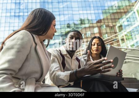 Diverse business team meets outdoors in an urban setting, sharing ideas over a laptop while discussing strategy, collaboration and remote communicatio Stock Photo