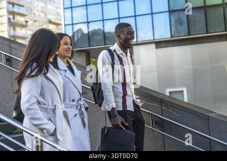 Diverse co workers and friends laughing and having a pleasant conversation while descending outdoor stairs in a modern urban environment, enjoying the Stock Photo