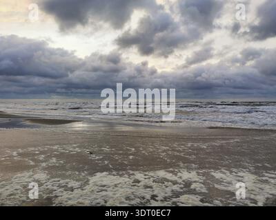 Dramatic sky over the sea at dusk with clouds and waves, foam along the coastline Stock Photo