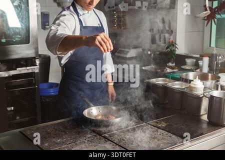 Chef Prepares Food in a Busy Kitchen While Steam Rises From the Stove During Lunch Hours Stock Photo