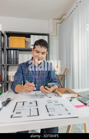 A young architect works on house design plans at his desk, focusing on drawings and scale models. The scene conveys creativity, dedication, and precis Stock Photo
