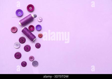 Different buttons and thread spools on lilac background Stock Photo