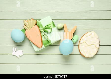 Gift box, eggs, Easter cookies in shape of egg and carrot on green wooden background Stock Photo