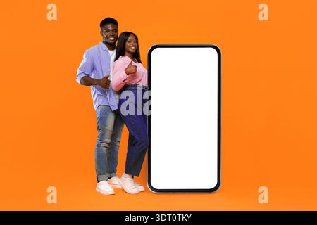 Couple Stands Together Next to a Large Smartphone on a Bright Orange Background Stock Photo