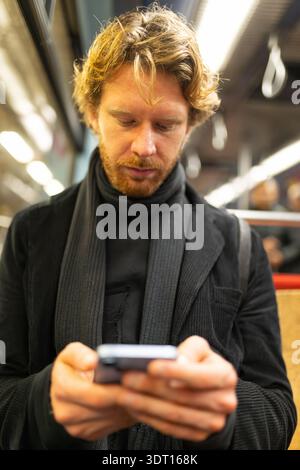 Red haired man commuting using smartphone in subway Stock Photo