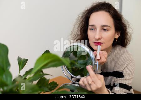 Woman applying lipstick using handheld mirror. Space for text. Stock Photo