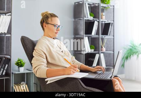 Young professional woman with glasses studying and working on laptop at home Stock Photo