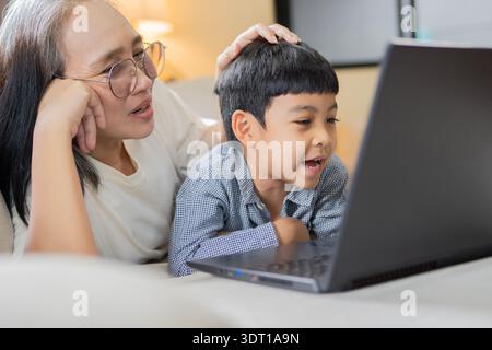 Happy middle age woman playing with her little son at home. They are using laptop computer for playing, learning and online surfing. Stock Photo