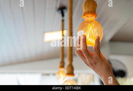 Decorative antique edison style filament light bulbs hanging. An electrician is installing spotlights on the ceiling. Close-up, selective focus. Stock Photo