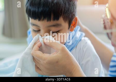 Mother support her son blowing nose with tissue for sneeze, flu or cold for virus, fever or sinus at home. Close-up, selective focus. Stock Photo