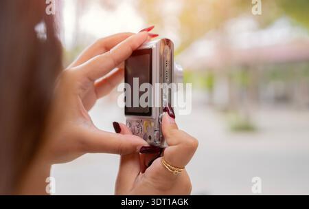 Young Asian woman traveler using digital compact camera, enjoying street cultural local place. Rear view, selective focus. Stock Photo