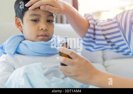 Mother giving cough syrup to her son ill with flu, Cute boy with his mom holding bottle with cough syrup in bed. Effective medicine. Selective focus. Stock Photo