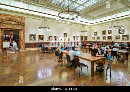 People are seated at tables in the reading room of a public library in Manhattan. They are studying and working on computers. Stock Photo