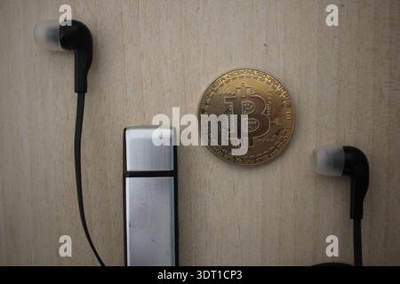 Concept of secure cryptocurrency storage featuring a Bitcoin, data pen drive, and modern headphones on a desk. Stock Photo