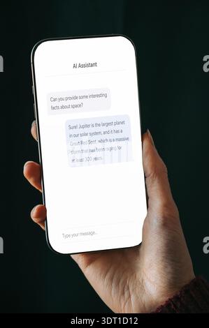 Close-up of a hand holding a smartphone with a clean AI assistant chat interface on screen. Minimal modern UI with chat bubbles and input field, ideal Stock Photo