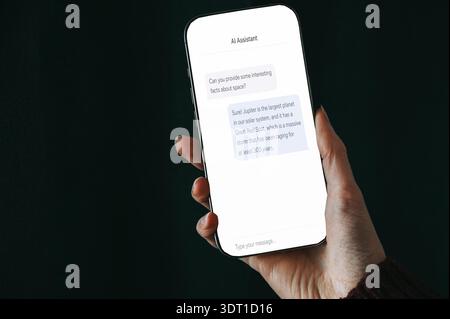Close-up of a hand holding a smartphone displaying an AI assistant chat conversation. Modern mobile technology concept for artificial intelligence, di Stock Photo