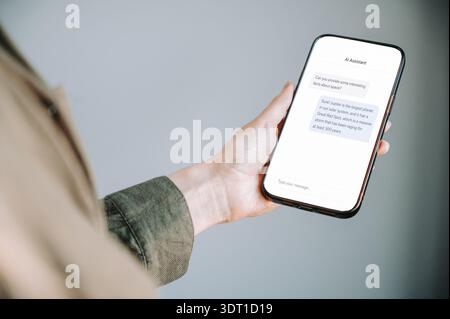 Close-up of a woman holding a smartphone displaying an AI assistant chat conversation. Modern artificial intelligence, mobile communication and digita Stock Photo