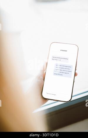 Close-up of a hand holding a smartphone displaying a modern AI assistant chat interface. Clean minimal design with chat bubbles and input field, ideal Stock Photo