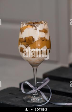 A beautifully layered dessert parfait in a wine glass featuring creamy white mousse, golden custard, chocolate crumbles, and a delicate ribbon accent Stock Photo