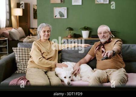 Senior Caucasian Couple Relaxing on Sofa with Dog While Watching Television Stock Photo