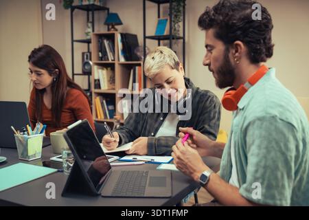 A group of diverse young professionals work together in a casual home office environment, brainstorming ideas and collaborating on a project using dig Stock Photo