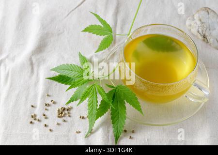 Cup of hot fresh cannabis tea with  branch and seeds on  hemp canvas fabric table cloth. Relaxation with herbal drink Stock Photo