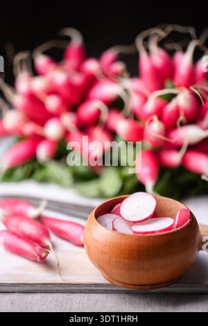 Wooden bowl with sliced radishes and fresh bunch on light background. Natural vegetables for minimalist food styling and healthy cuisine Stock Photo