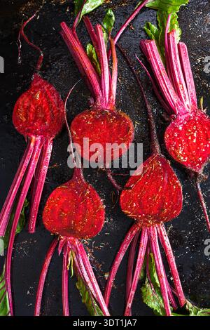 Raw beetroot slices arranged on dark background prepared for roasting with oil and spices. Fresh vegetable food composition with vibrant colors Stock Photo
