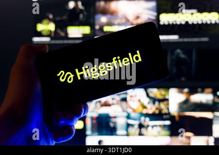 Hand holding smartphone displaying Higgsfield AI logo on screen with blurred website background, generative artificial intelligence video creation and Stock Photo