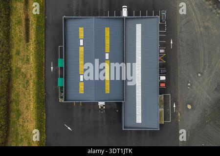 Aerial view of a building with yellow stripes on its roof contrasting against the dark asphalt and green grass, Tréglamus, Bretagne, France. Stock Photo
