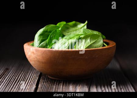 Baby spinach leaves in handmade wooden bowl on vintage wooden tabletop with black background. Organic harvest, healthy cooking and farm to table concept Stock Photo