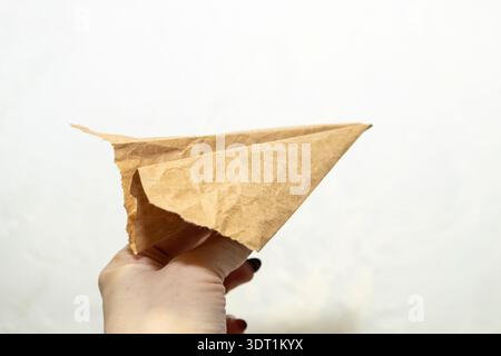 Hand of the woman hold origami plane from old brown paper against background. Stock Photo