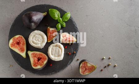 Sliced sweet figs and goat cheese on round dark stone slate board - healthy diet. Top view with copy space Stock Photo