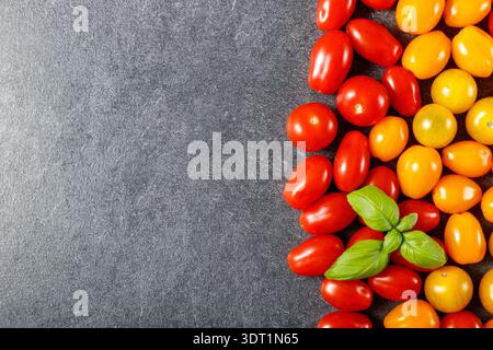 Mixed color cherry tomatoes with basil leaves  top view on grey stone background with copy space. Red, orange and yellow cherry tomato Stock Photo