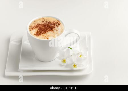 Empty porcelain coffee cup with saucer decorated orchid flowers in trendy color of 2026 year Cloud Dancer on light background. Cloud Dancer color back Stock Photo