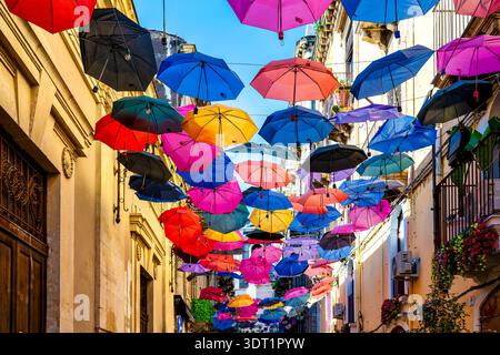 Colorful umbrellas suspended above Via Gisira in Catania, Sicily, Italy with clear blue sky. Stock Photo