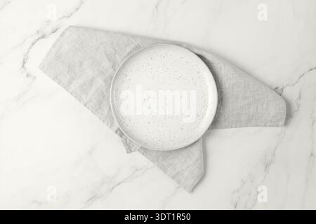 Empty craftmade vintage white plate on folded light grey soft pure linen serviette  over marble table or board. Cuisine dishware mockup with copy spac Stock Photo