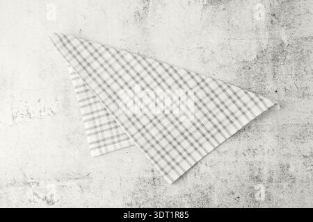 Folded light grey plaid cotton towel on empty grunge stone board. Trendy color of 2026 year Cloud Dancer. Stock Photo