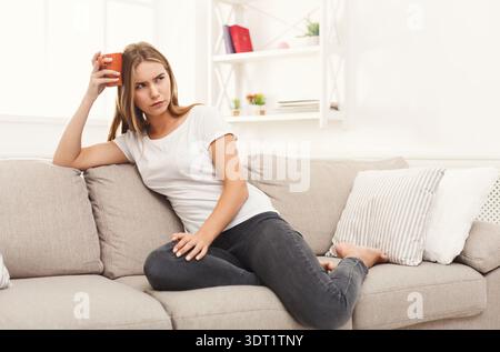 Woman Sitting on Couch With Phone Looking Bored and Lost in Thought Stock Photo
