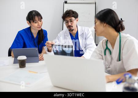 A medical team discussing patient care, featuring one nurse in white and two doctors, collaboratively reviewing X-rays and charts in a professional he Stock Photo