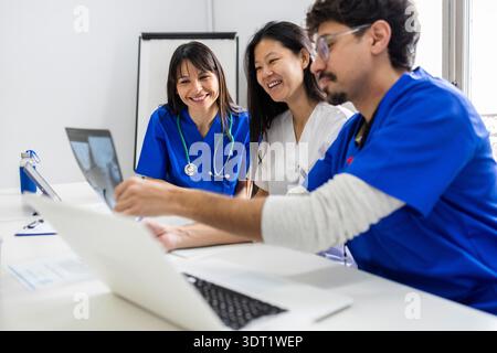 A dedicated medical team, including two doctors and a nurse in white uniforms, collaborates closely in a clinical setting while reviewing patient reco Stock Photo