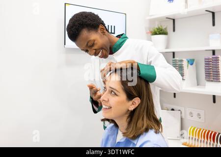 An optician comfortably assists a woman in placing contact lenses at an eye care clinic. The scene conveys professional care in a contemporary healthc Stock Photo