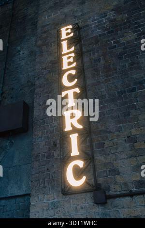 A vintage neon sign reading Electric glows warmly against an old brick wall. The industrial setting and weathered textures evoke a nostalgic urban atm Stock Photo