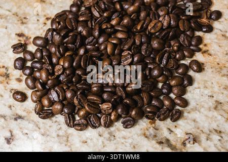 Freshly roasted coffee beans scattered across a marble surface, showcasing their rich color and texture. Perfect for a morning brew, adding warmth to Stock Photo