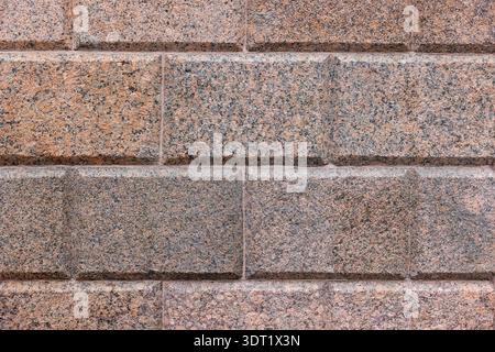 A close-up view of a red gray, speckled granite block wall with beveled joints and rough texture. Ideal for architectural backdrops, construction visu Stock Photo
