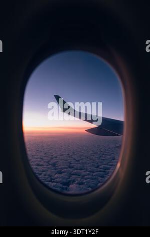 Airplane Wing Seen Through Window at Sunrise Above the Clouds Stock Photo
