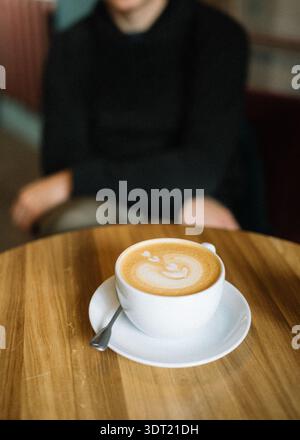 White cup of coffee with latte art on wooden table, man blurred Stock Photo